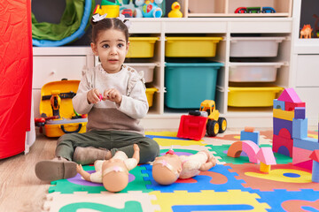 Wall Mural - Adorable hispanic girl sitting on floor playing with baby doll at kindergarten