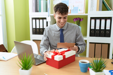 Wall Mural - Young hispanic man business worker unpacking gift holding letter at office