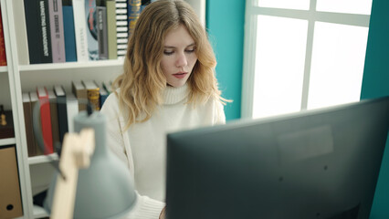 Young blonde woman student using computer studying at library university