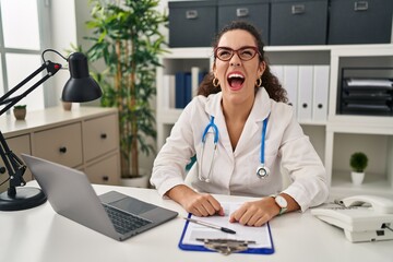 Sticker - Young hispanic woman wearing doctor uniform and stethoscope angry and mad screaming frustrated and furious, shouting with anger. rage and aggressive concept.