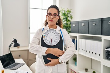 Canvas Print - Young hispanic woman working at dietitian clinic relaxed with serious expression on face. simple and natural looking at the camera.