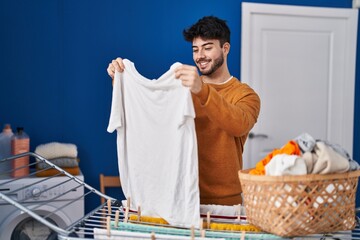 Wall Mural - Young hispanic man smiling confident hanging clothes on clothesline at laundry room