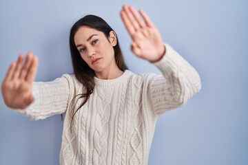 Sticker - Young brunette woman standing over blue background doing frame using hands palms and fingers, camera perspective