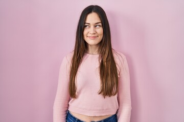 Wall Mural - Young brunette woman standing over pink background smiling looking to the side and staring away thinking.