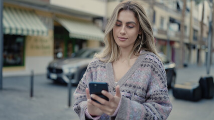 Poster - Young blonde woman using smartphone with relaxed expression at street