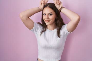 Poster - Young hispanic girl standing over pink background posing funny and crazy with fingers on head as bunny ears, smiling cheerful