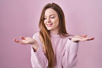 Poster - Young caucasian woman standing over pink background smiling showing both hands open palms, presenting and advertising comparison and balance