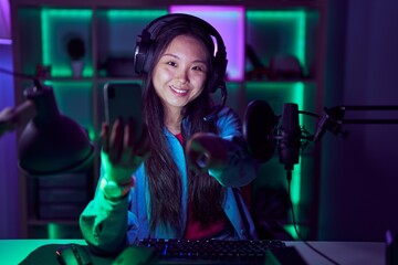 Poster - Young asian woman playing video games with smartphone pointing to you and the camera with fingers, smiling positive and cheerful