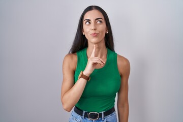 Wall Mural - Young woman standing over isolated background thinking concentrated about doubt with finger on chin and looking up wondering