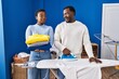 © Krakenimages.com - Young african american couple ironing clothes at laundry room smiling looking to the side and staring away thinking.