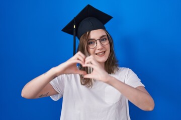 Poster - Blonde caucasian woman wearing graduation cap smiling in love doing heart symbol shape with hands. romantic concept.