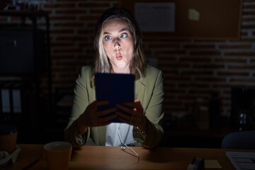 Wall Mural - Blonde caucasian woman working at the office at night making fish face with lips, crazy and comical gesture. funny expression.