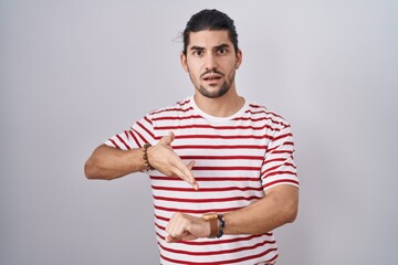 Wall Mural - Hispanic man with long hair standing over isolated background in hurry pointing to watch time, impatience, upset and angry for deadline delay