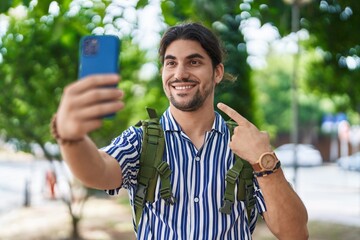 Wall Mural - Hispanic man with long hair outdoors at the city doing video call smiling happy pointing with hand and finger