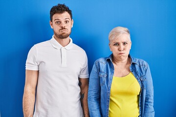 Poster - Young brazilian mother and son standing over blue background puffing cheeks with funny face. mouth inflated with air, crazy expression.