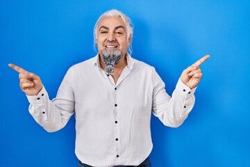 Poster - Middle age man with grey hair standing over blue background smiling confident pointing with fingers to different directions. copy space for advertisement