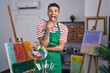 Brazilian young man holding painter palette at artist studio sticking tongue out happy with funny expression.
