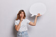 canvas print picture - Pensive young European woman holds chin and looks doubtful holds blank speech communication bubble thinks what text to write dressed in casual t shirt and jeans isolated over white background.