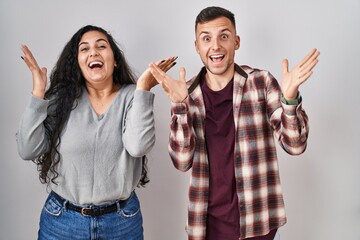 Sticker - Young hispanic couple standing over white background celebrating crazy and amazed for success with arms raised and open eyes screaming excited. winner concept