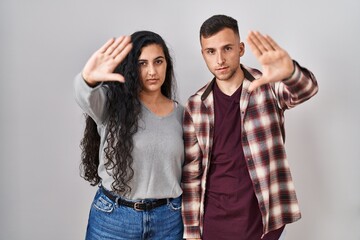 Poster - Young hispanic couple standing over white background doing frame using hands palms and fingers, camera perspective