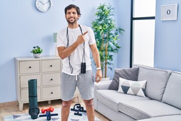 Wall Mural - Handsome latin man wearing sportswear at home cheerful with a smile of face pointing with hand and finger up to the side with happy and natural expression on face