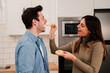 © Jose Calsina - Young couple eating together in affeccionate attitude. Two people laugh and feed each other at home kitchen. Smiling wife flirting giving healthy food to her handsome husband having a romantic lunch