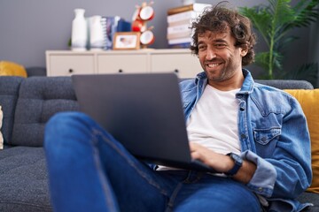 Poster - Young hispanic man using laptop sitting on sofa at home