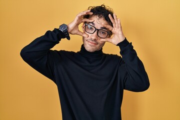 Poster - Hispanic man standing over yellow background trying to open eyes with fingers, sleepy and tired for morning fatigue