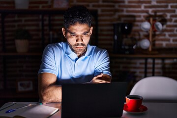 Canvas Print - Hispanic man with beard using laptop at night skeptic and nervous, disapproving expression on face with crossed arms. negative person.