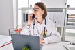 © Krakenimages.com - Young caucasian woman doctor using laptop talking on smartphone at clinic
