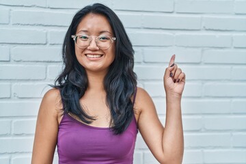 Wall Mural - Asian young woman standing over bricks background smiling happy pointing with hand and finger to the side