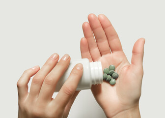 Wall Mural - woman puts green herbal organic pills from a white jar in her palm. taking medicines, natural detox drugs concept