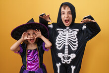 Adorable Boy And Girl Wearing Halloween Costume Doing Fear Gesture Over Isolated Yellow Background