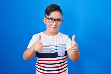 Poster - Young hispanic kid standing over blue background pointing fingers to camera with happy and funny face. good energy and vibes.