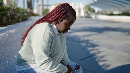 Canvas Print - African woman with braided hair looking sad sitting on a bench at park