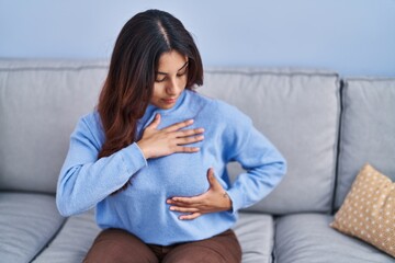 Young hispanic woman examining breast touching with hands at home