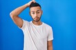 © Krakenimages.com - Young hispanic man standing over blue background confuse and wondering about question. uncertain with doubt, thinking with hand on head. pensive concept.