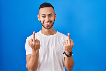 Poster - Young hispanic man standing over blue background showing middle finger doing fuck you bad expression, provocation and rude attitude. screaming excited