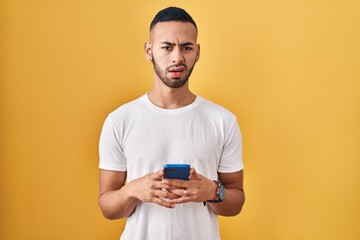 Canvas Print - Young hispanic man using smartphone typing message clueless and confused expression. doubt concept.