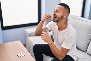 Canvas Print - African american man taking pills sitting on sofa at home