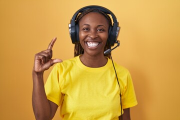 Canvas Print - African american woman listening to music using headphones smiling and confident gesturing with hand doing small size sign with fingers looking and the camera. measure concept.