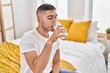 © Krakenimages.com - Young hispanic man drinking glass of water sitting on bed at bedroom