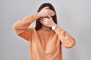 Canvas Print - Young brunette woman standing over white background covering eyes and mouth with hands, surprised and shocked. hiding emotion