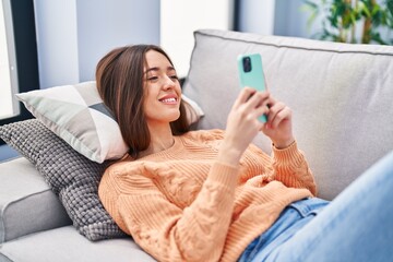 Poster - Young beautiful hispanic woman using smartphone lying on sofa at home