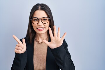 Canvas Print - Young brunette woman standing over blue background showing and pointing up with fingers number seven while smiling confident and happy.