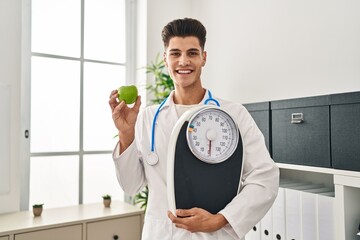 Wall Mural - Young hispanic doctor man holding scale at dietitian clinic smiling with a happy and cool smile on face. showing teeth.