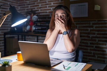 Poster - Brunette woman working at the office at night shocked covering mouth with hands for mistake. secret concept.