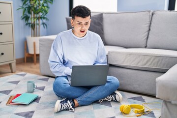 Poster - Non binary person studying using computer laptop sitting on the floor afraid and shocked with surprise expression, fear and excited face.