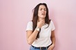 Young brunette woman standing over pink background touching painful neck, sore throat for flu, clod and infection