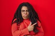 Plus size hispanic woman standing over red background pointing aside worried and nervous with forefinger, concerned and surprised expression